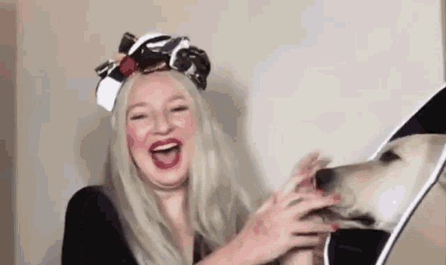 a woman is laughing while holding a dog 's head in front of a mirror .