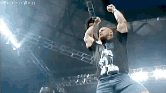 a wrestler is raising his fist in the air while wearing a black shirt with the number 32 on it .