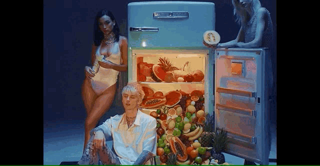 a man is sitting in front of a refrigerator filled with fruit and vegetables .