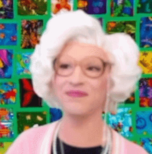 a woman with white hair and glasses is standing in front of a colorful background