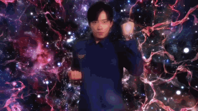 a man in a blue shirt is holding a heart in his hands in front of a galaxy .