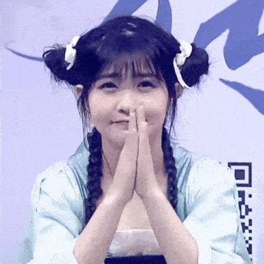 a girl with braids is making a funny face with her hands folded in front of her face
