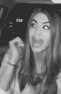 a black and white photo of a woman making a funny face while sitting in a car .