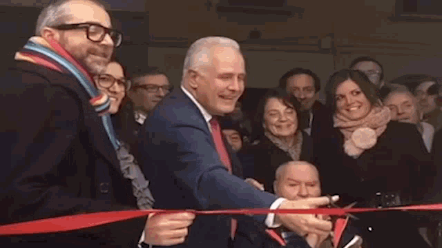 a man is cutting a red ribbon in front of a crowd .