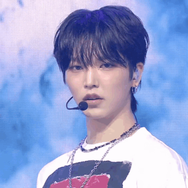 a young man wearing a white shirt and a microphone looks at the camera