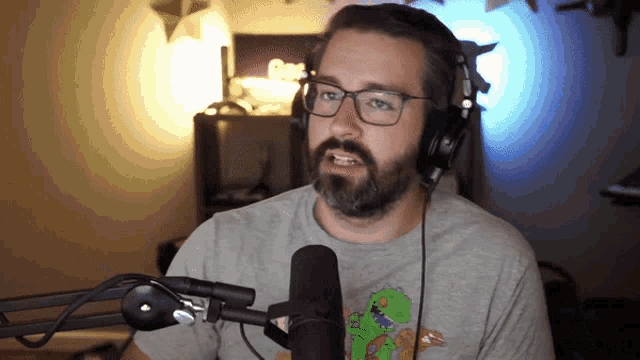 a man wearing headphones and a t-shirt with a dinosaur on it is speaking into a microphone
