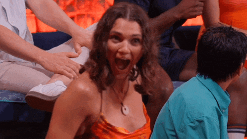 a woman in an orange dress is sitting on a couch with her mouth open