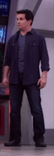a man in a blue shirt and blue jeans is standing in front of a wall .