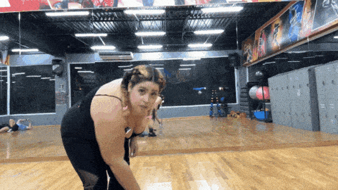 a woman stands in front of a mirror in a gym with a sign that says ' lockers ' on it
