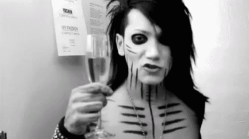 a man with black paint on his face is holding a glass of wine .