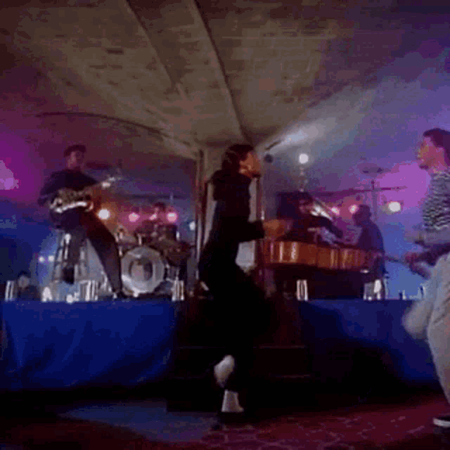 a woman in a black turtleneck is dancing on a stage in front of a drum set .