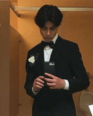 a man in a tuxedo and bow tie is taking a selfie in a bathroom .