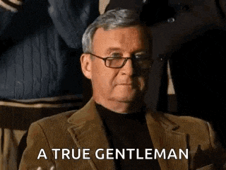 a man in a suit and glasses is sitting in a chair with the words `` a true gentleman '' written below him .