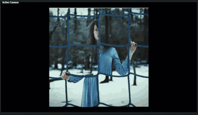 a woman in a blue dress is standing behind a blue net with the words active camera visible