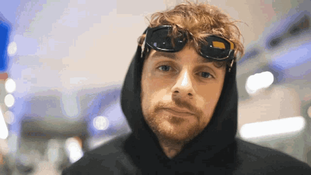 a man wearing sunglasses and a black hoodie is looking at the camera