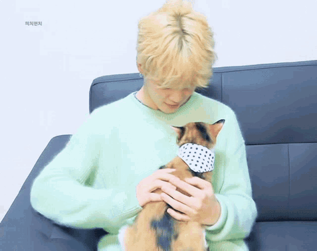 a man in a green sweater is holding a cat with a bandana on it