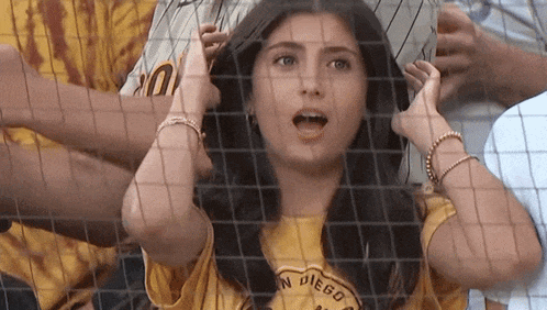 a woman wearing a yellow shirt that says san diego is behind a fence