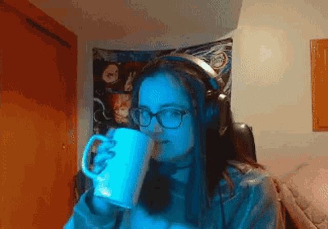 a girl wearing headphones and glasses is drinking from a mug .