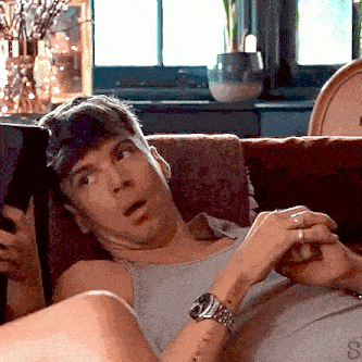 a man laying on a couch looking at a tablet with the letter s on his wrist