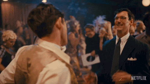a man in a suit and tie is talking to another man in a crowded room .