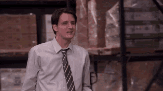 a man in a shirt and tie is standing in a warehouse with boxes in the background