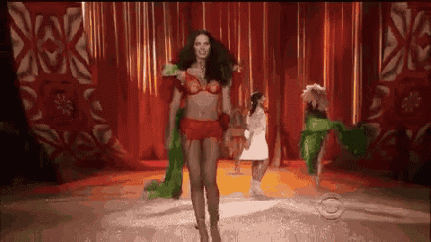a woman is walking down a runway at a fashion show wearing a red bra and shorts .