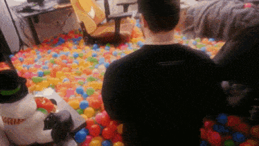 a man in a black shirt stands in a ball pit filled with colorful balls