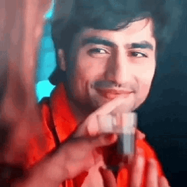 a man in a red shirt is holding a shot glass in his hand and making a funny face .