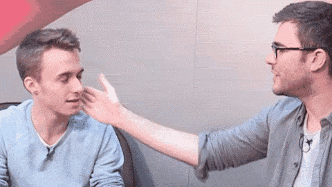two men are sitting next to each other and one of them is touching the face of the other .