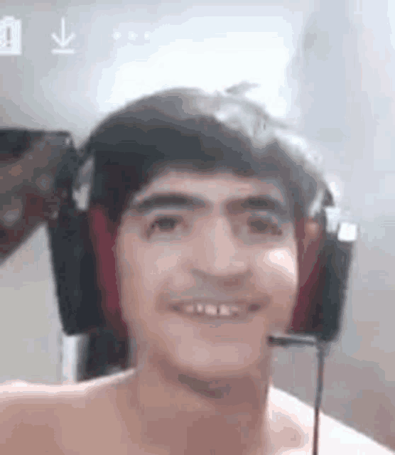 a shirtless young man wearing headphones and a microphone is smiling .