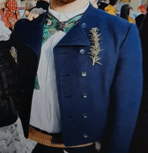 a man wearing a blue jacket has a rosemary leaf pinned to his jacket