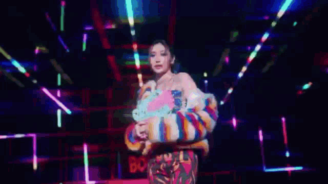 a woman in a colorful dress is standing in a dark room surrounded by neon lights .