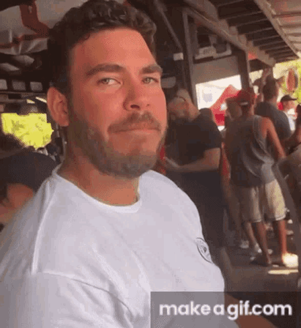 a man with a beard wearing a white shirt is standing in front of a crowd of people .