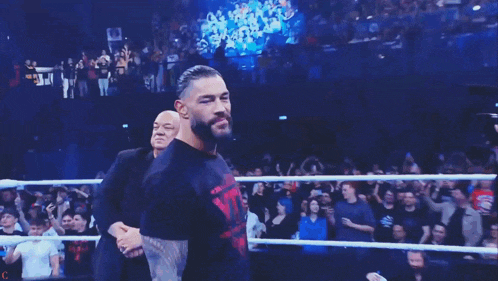 a man with a beard is walking in a boxing ring with a crowd behind him .