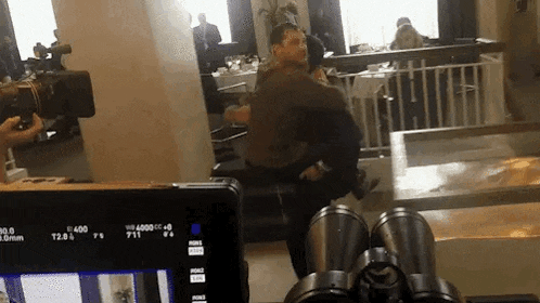 a man is carrying another man in his arms in a room with binoculars in front of a camera .