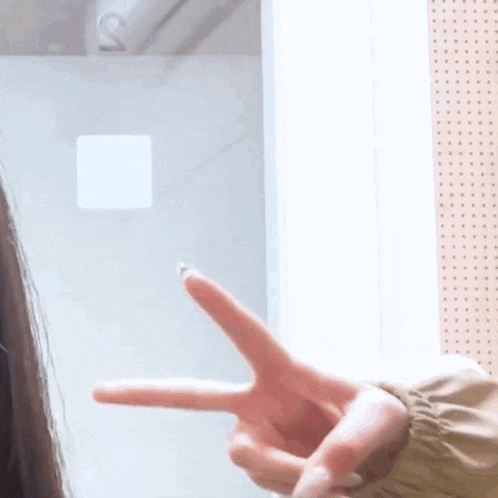 a woman is making a peace sign with her fingers in front of a window .