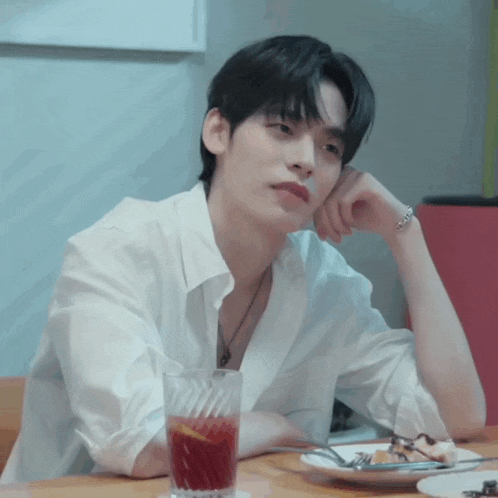 a man in a white shirt is sitting at a table with a plate of food and a glass of juice .