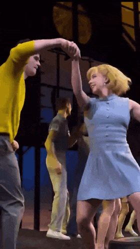 a woman in a blue dress is dancing with a man in a yellow shirt on a stage