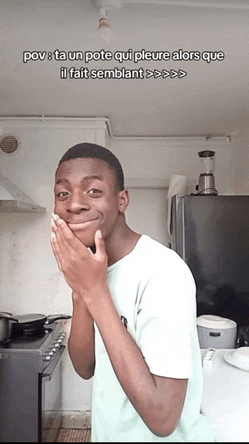 a young man covering his mouth with his hands in front of a blender and a stove