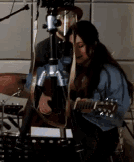 a woman is playing a guitar in front of a man playing drums