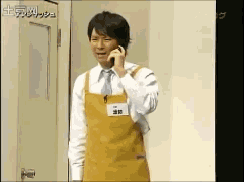 a man wearing a yellow apron talking on a cell phone