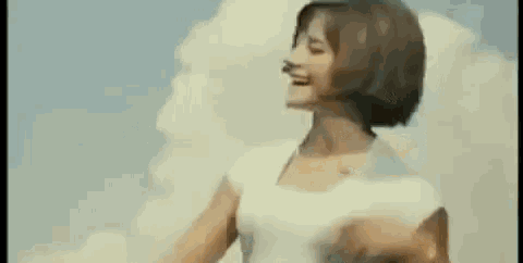 a woman in a white shirt is dancing in front of a blue sky with clouds .