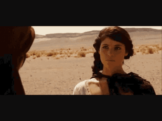 a woman is standing in the desert looking at a horse