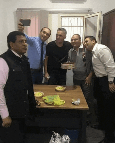 a group of men are posing for a picture with a cake on the table