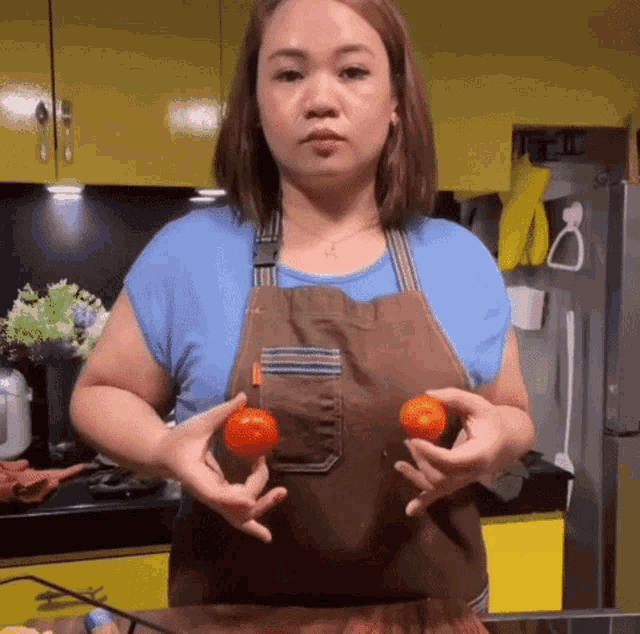 a woman in a brown apron is holding two tomatoes in her hands