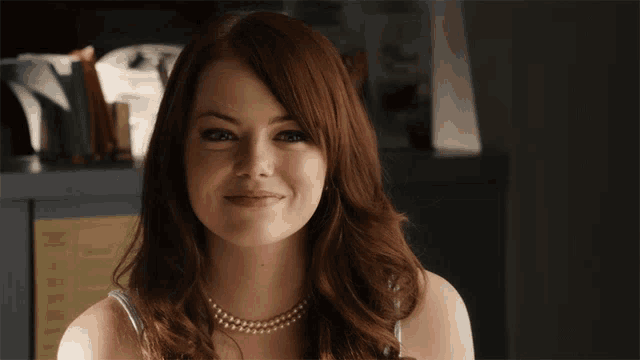 a woman wearing a pearl necklace smiles for the camera