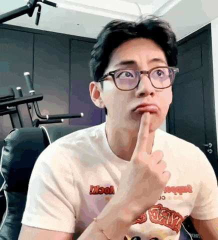 a man wearing glasses and a white t-shirt is making a funny face with his finger to his mouth .