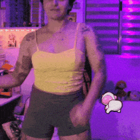a woman in a yellow tank top and shorts is dancing in front of a purple background