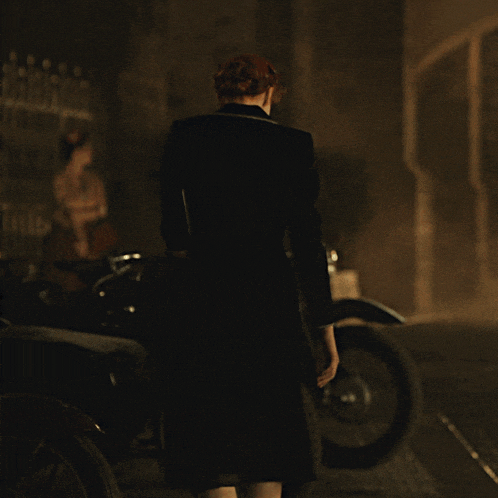 a woman in a black dress stands in front of a motorcycle with a license plate that reads hk