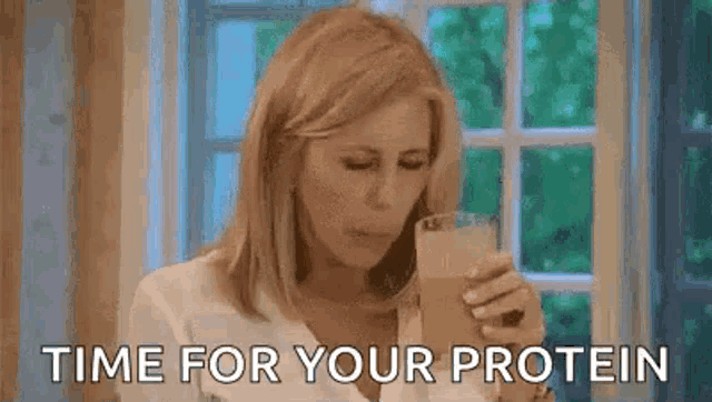 a woman is drinking a protein shake in front of a window while talking on a cell phone .